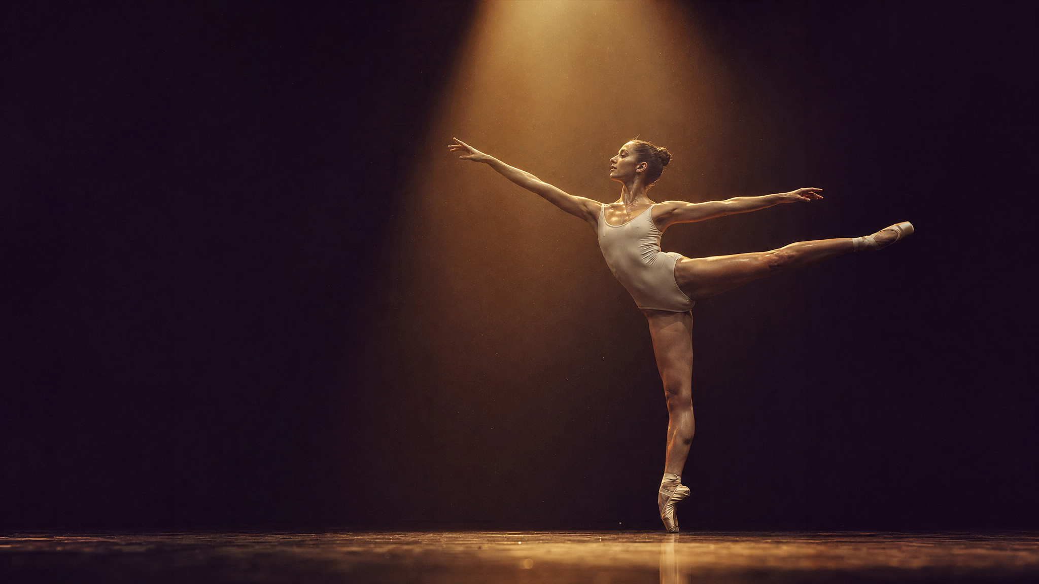 Ballet dancer in arabesque, dramatic spotlight on dark stage