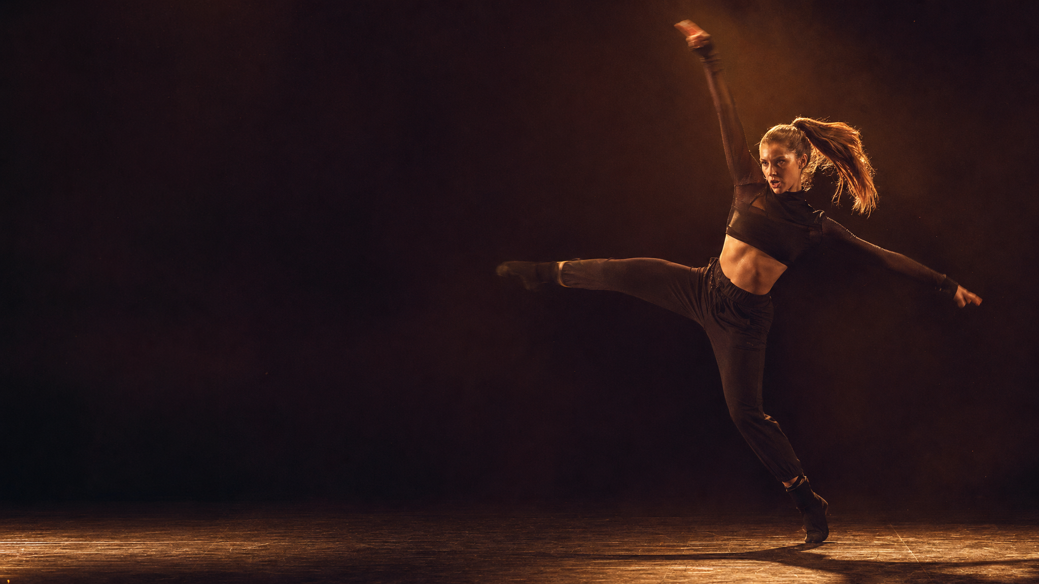 Jazz dancer in sharp angular pose, warm spotlight on dark stage